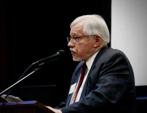 Older man with white hair speaking at a podium with a microphone.